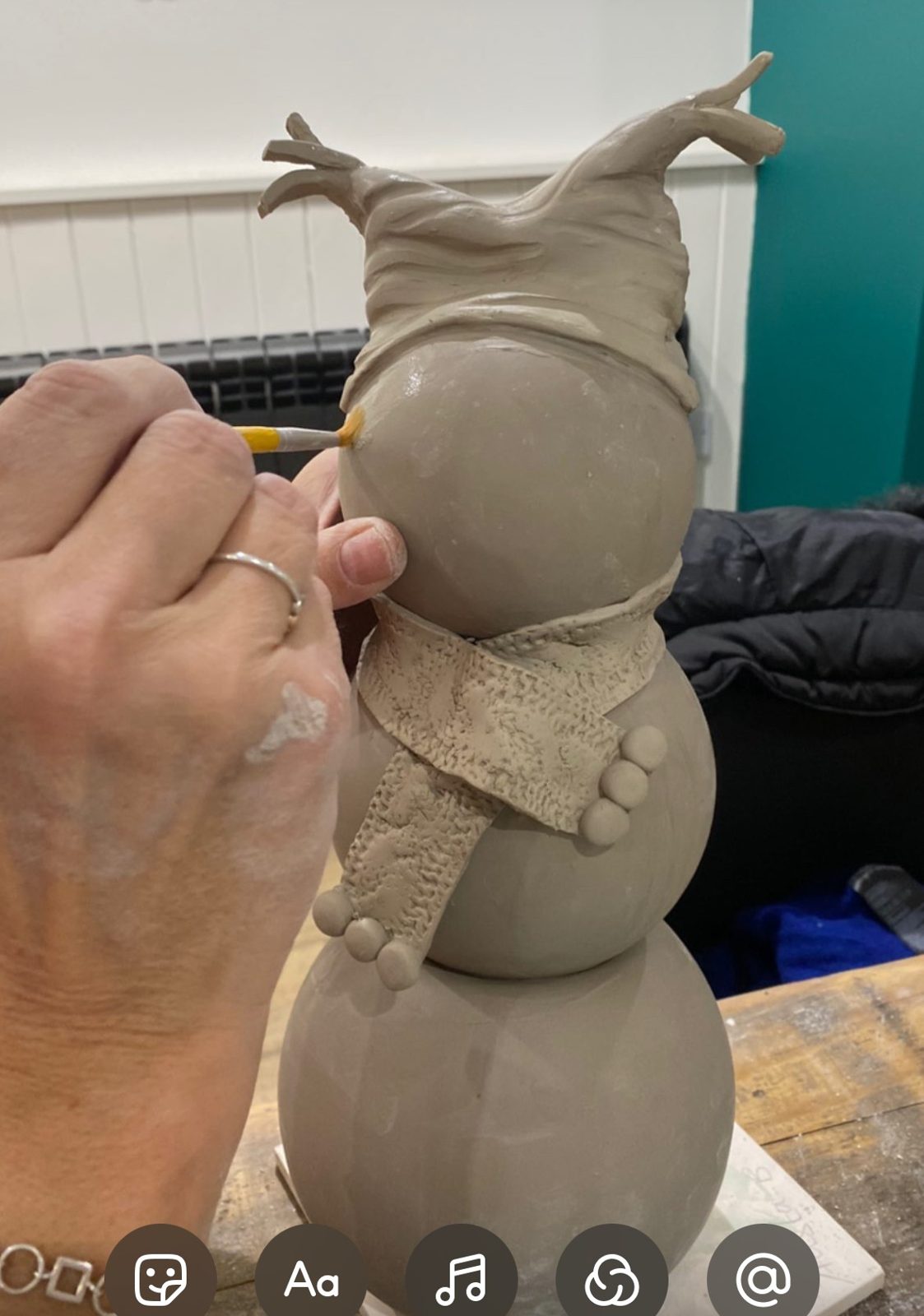 Hands wrapping a clay scarf around a snowman