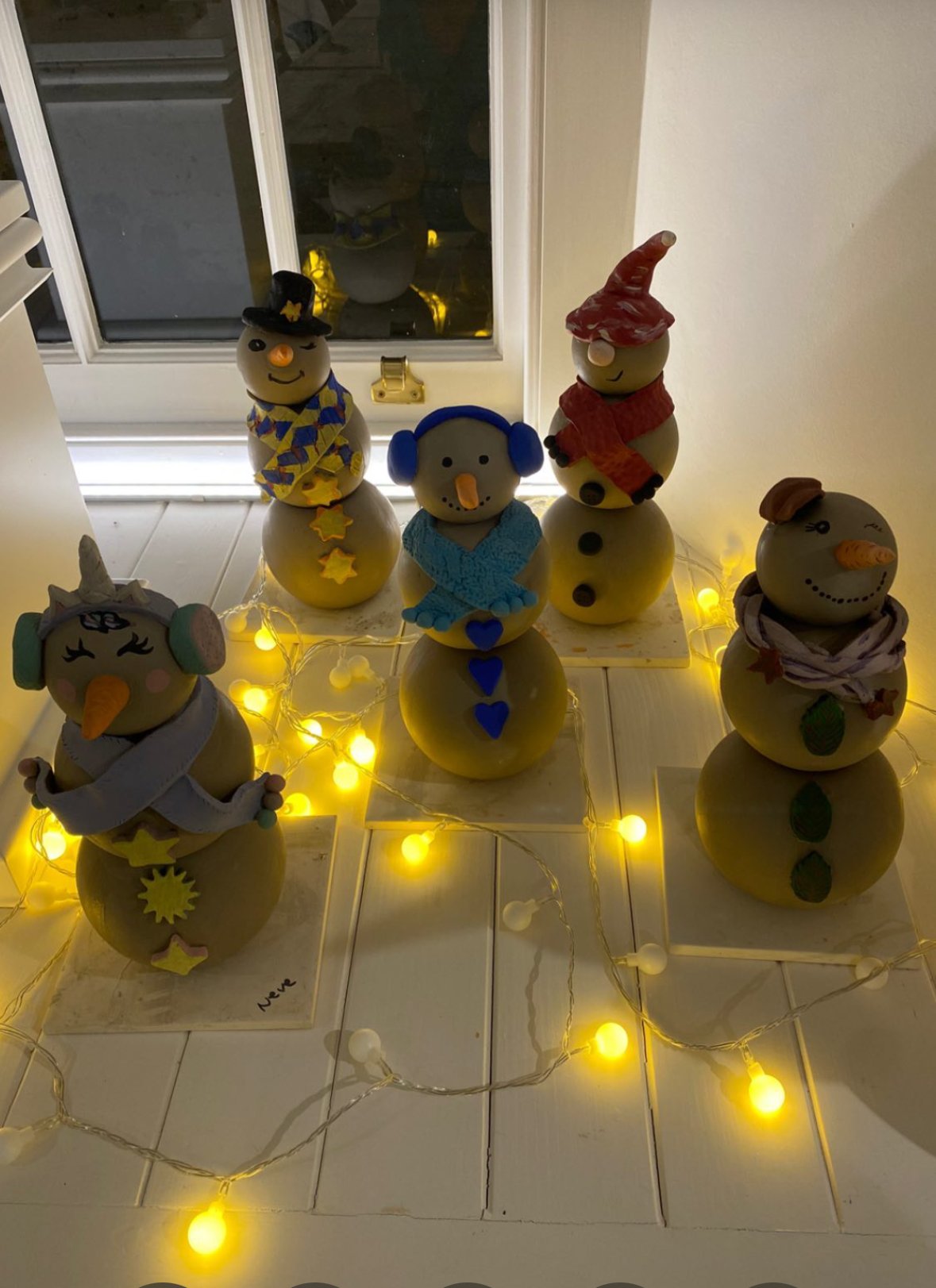 The finished clay snowmen dressed in scarves, among fairy lights